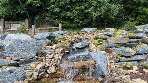 A naturalistic water feature with a cascading waterfall, surrounded by rocks and plants, and a sign indicating 'The Falls at Bartlett Glen Cove.' - Mountain Breeze (Bryson City)