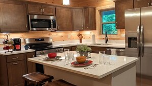 A modern kitchen with wooden cabinets, stainless steel appliances, a central island with stools, and pendant lighting. - Mountain Breeze (Bryson City)