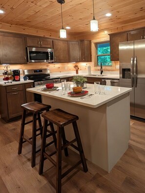 Une cuisine moderne avec des meubles en bois, des appareils en acier inoxydable, un îlot central doté de tabourets et un éclairage suspendu.