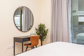 Ein Hotelzimmer mit Bett, Schreibtisch, Stuhl, Spiegel, Pflanze und einem Fenster mit Vorhängen.