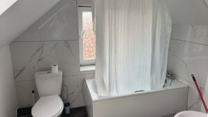 Kylpyhuone, jossa on wc, kylpyamme ja suihkuverho.