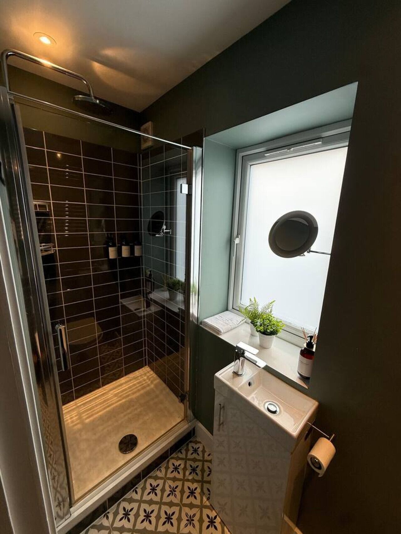 Une petite salle de bain comprenant une douche, un lavabo, des toilettes et une fenêtre agrémentée d’une plante.