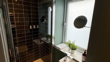 Une petite salle de bain comprenant une douche, un lavabo, des toilettes et une fenêtre agrémentée d’une plante.