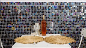 Ein Tisch mit zwei gewebten Tischsets, einer Flasche und zwei Gläsern vor einer Wand mit Mosaikfliesen.