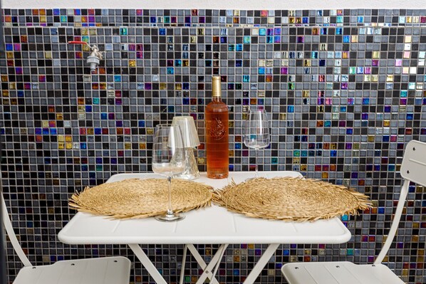 A table with two woven placemats, a bottle, and two glasses against a mosaic tile wall. - Tavira Bliss Garden Apartment (Tavira)