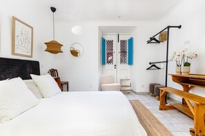 A bedroom with a bed, a chair, a desk, a hanging light, a mirror, and a door with blue curtains. - Tavira Bliss Garden Apartment (Tavira)