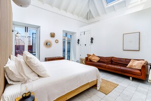Een slaapkamer met een groot bed, een bruine leren bank, een kleine tafel en een wandlamp.