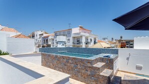 Ein Dachpool mit einer gefliesten Kante, umgeben von Gebäuden mit Balkonen und einem klaren Himmel.