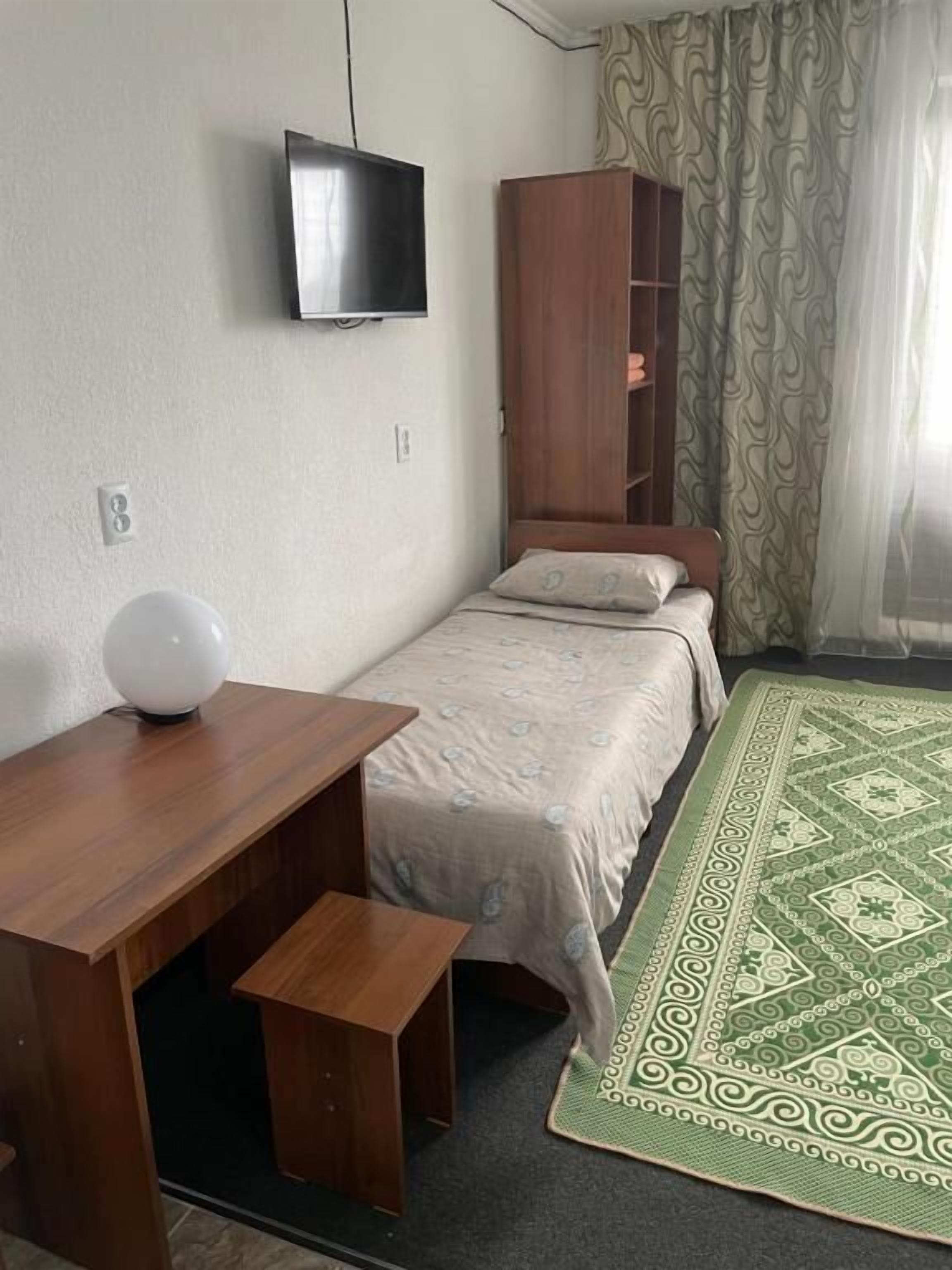 A bedroom with a bed, a wooden desk, a television, and a wardrobe.
