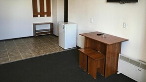 A small kitchenette with a refrigerator, a microwave, and a sink. There is a wooden bench and a small table with a remote control on it.