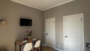 A room with a wooden floor, a table with chairs, a flat-screen TV, and two white doors.