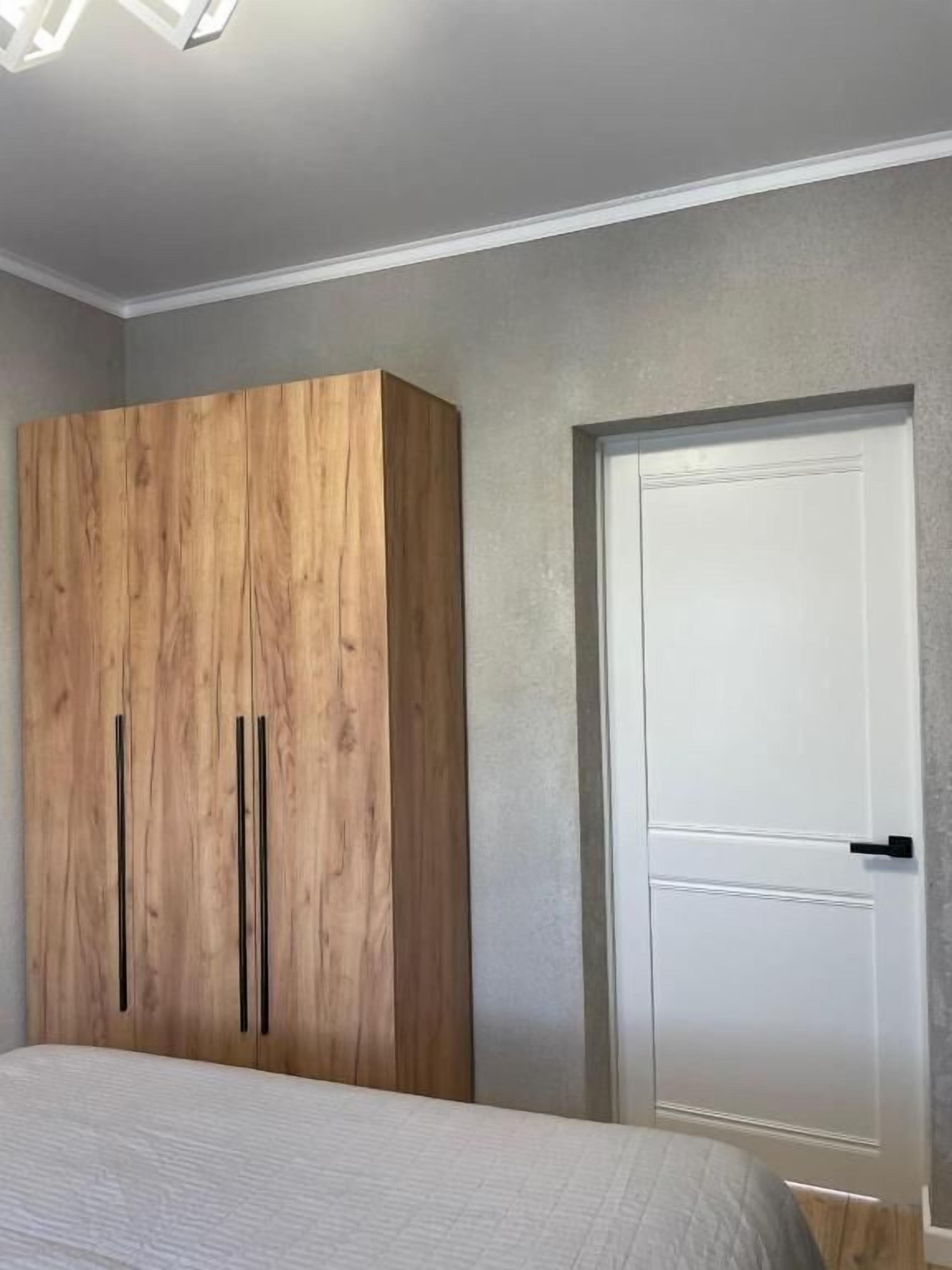 Un dormitorio con una cama, un armario de madera y una puerta blanca.