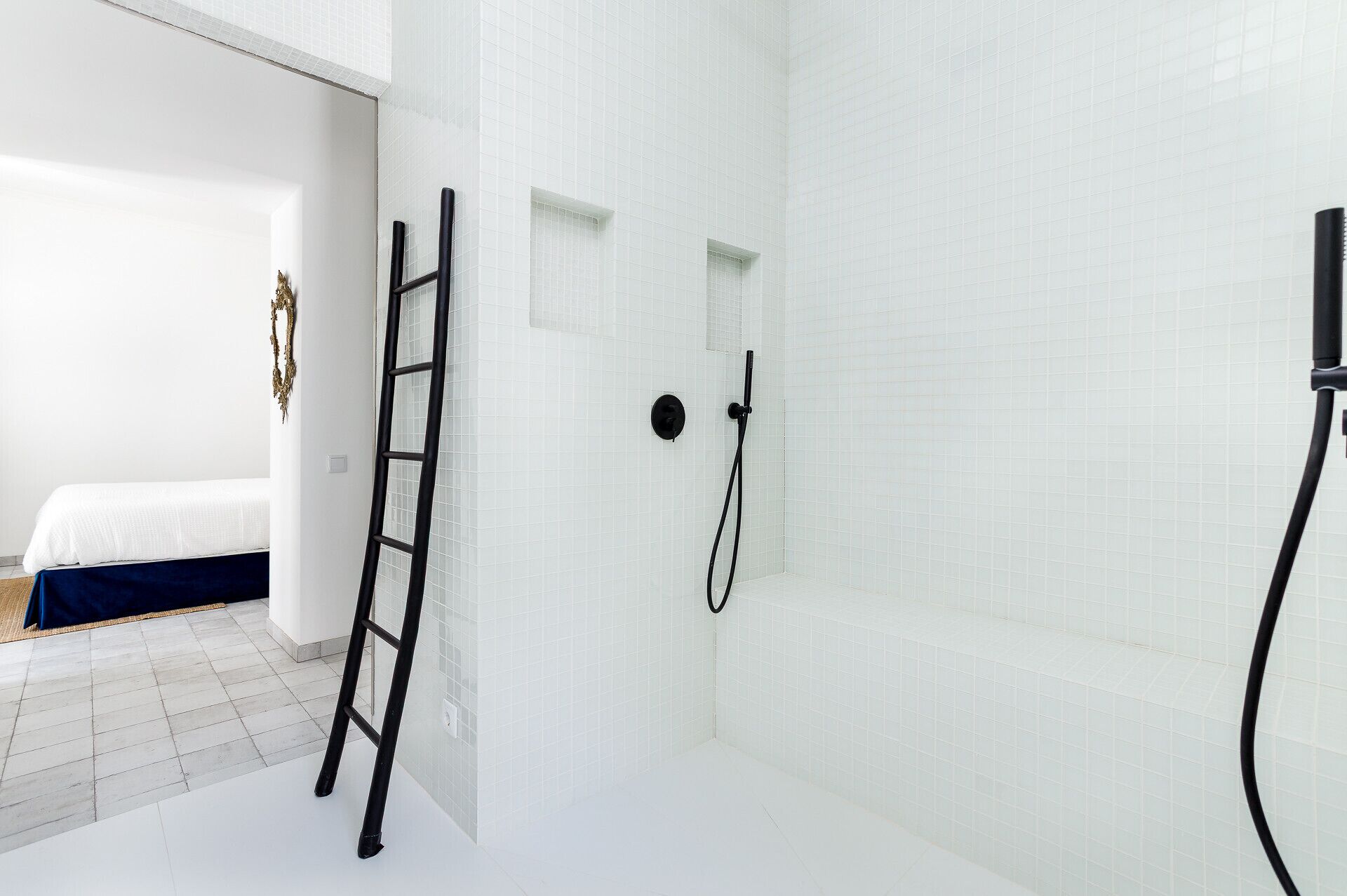 A modern bathroom with white tiled walls, a shower, and a ladder.