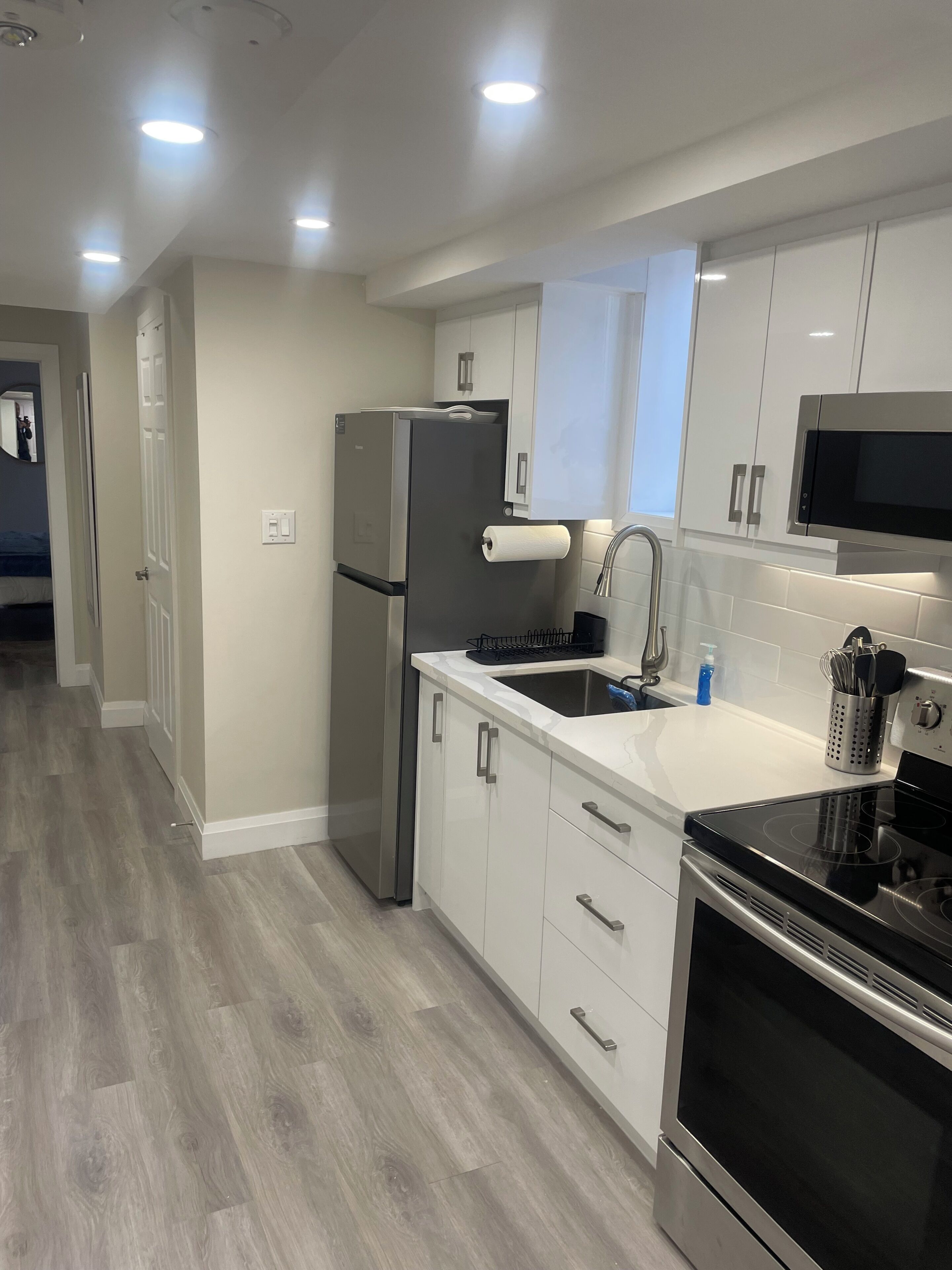 A modern kitchen with white cabinets, stainless steel appliances, and a wooden floor.