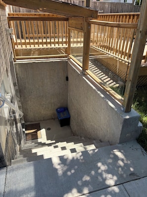 Eine Betonkonstruktion mit Holzdeck, Treppen zu einem überdachten Bereich und einem kleinen, blauen Gegenstand am Boden.