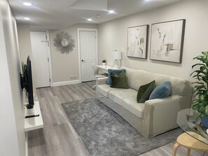 A modern living room with a sofa, a glass coffee table, and artwork on the wall. - The Whitby Hideaway - a modern space on a quiet stree wih a private patio area. (Whitby)
