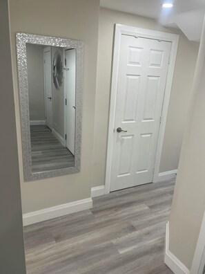 A hallway with a white door, a mirror with a textured frame, and a light fixture on the ceiling. - The Whitby Hideaway - a modern space on a quiet stree wih a private patio area. (Whitby)