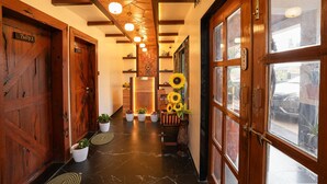 A hallway with wooden doors, potted plants, a reception desk, and a large window with a view of the street. - Sunflower Vista - 6BR Estate with Pool, Hot Tub & Hill Views, Mahabaleshwar (Panchgani)