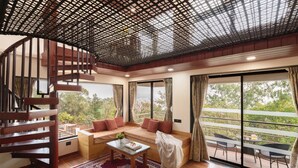 A modern interior with a wooden staircase, a sofa set, a coffee table, and a balcony with outdoor seating. - Sunflower Vista - 6BR Estate with Pool, Hot Tub & Hill Views, Mahabaleshwar (Panchgani)