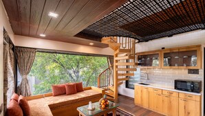A modern interior with a wooden staircase, a kitchen with wooden cabinets, a seating area with a sofa, and a large window with a view of trees. - Sunflower Vista - 6BR Estate with Pool, Hot Tub & Hill Views, Mahabaleshwar (Panchgani)