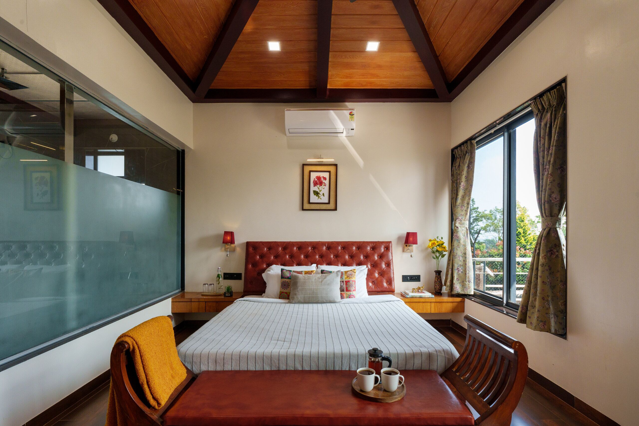 Habitación de hotel con una cama grande, techo de madera, ventana con cortinas y una mesa con una bandeja de tazas.