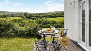 An outdoor patio with a round table, chairs, and a bottle of wine, overlooking a lush green landscape. - The Vineyard at Newton Court, Nr Monmouth sleeps 10 guests (Near Monmouth)