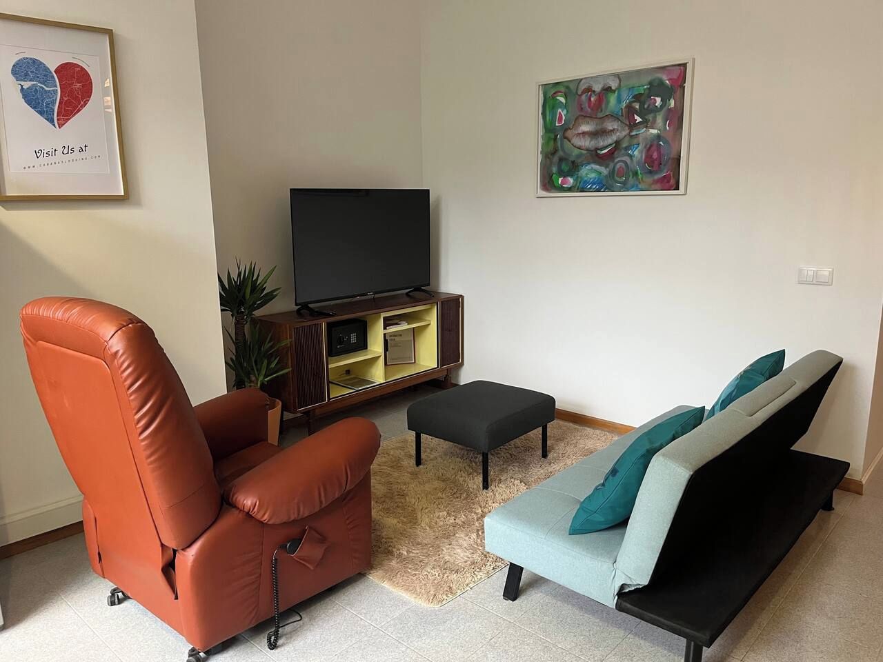 Un salon comprenant un fauteuil en cuir, un canapé avec des coussins, un téléviseur à écran plat, une petite table et un tableau accroché au mur.