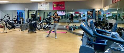 A gym with exercise equipment, mirrors, and a woman working out.