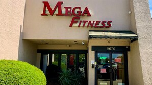 Fasaden på en Mega Fitness-byggnad med en stor skylt, en glasdörr och siffran 9676 på dörren.