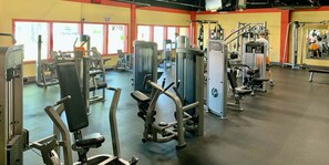 Ein Fitnessraum mit verschiedenen Trainingsgeräten, einer Spiegelwand und einem Schild, das einen Wartebereich kennzeichnet.