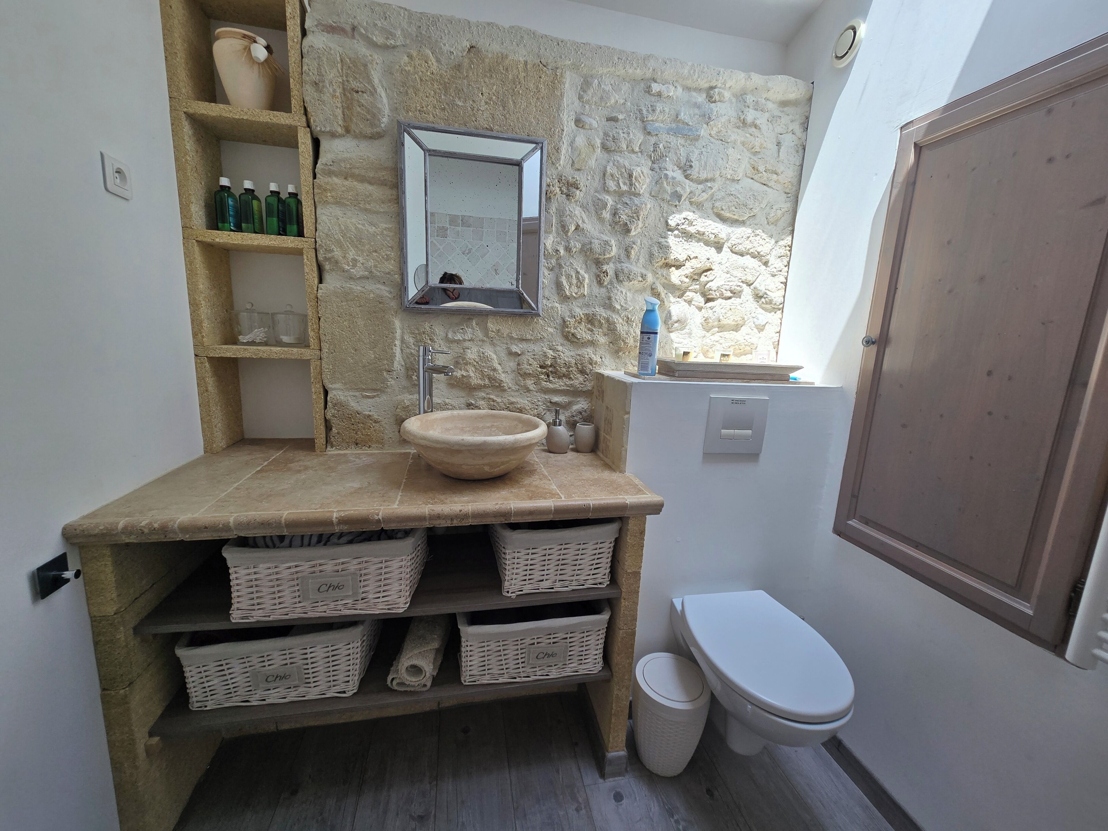 A bathroom with a stone wall, a sink, a mirror, and a toilet.