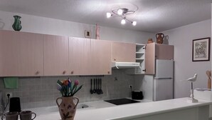 Une cuisine moderne avec des meubles de couleur rose pâle, un plan de travail blanc, un vase rempli de fleurs et un luminaire au plafond.