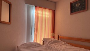 Une chambre avec deux lits, une fenêtre avec des rideaux, une lampe et un tableau encadré au mur.