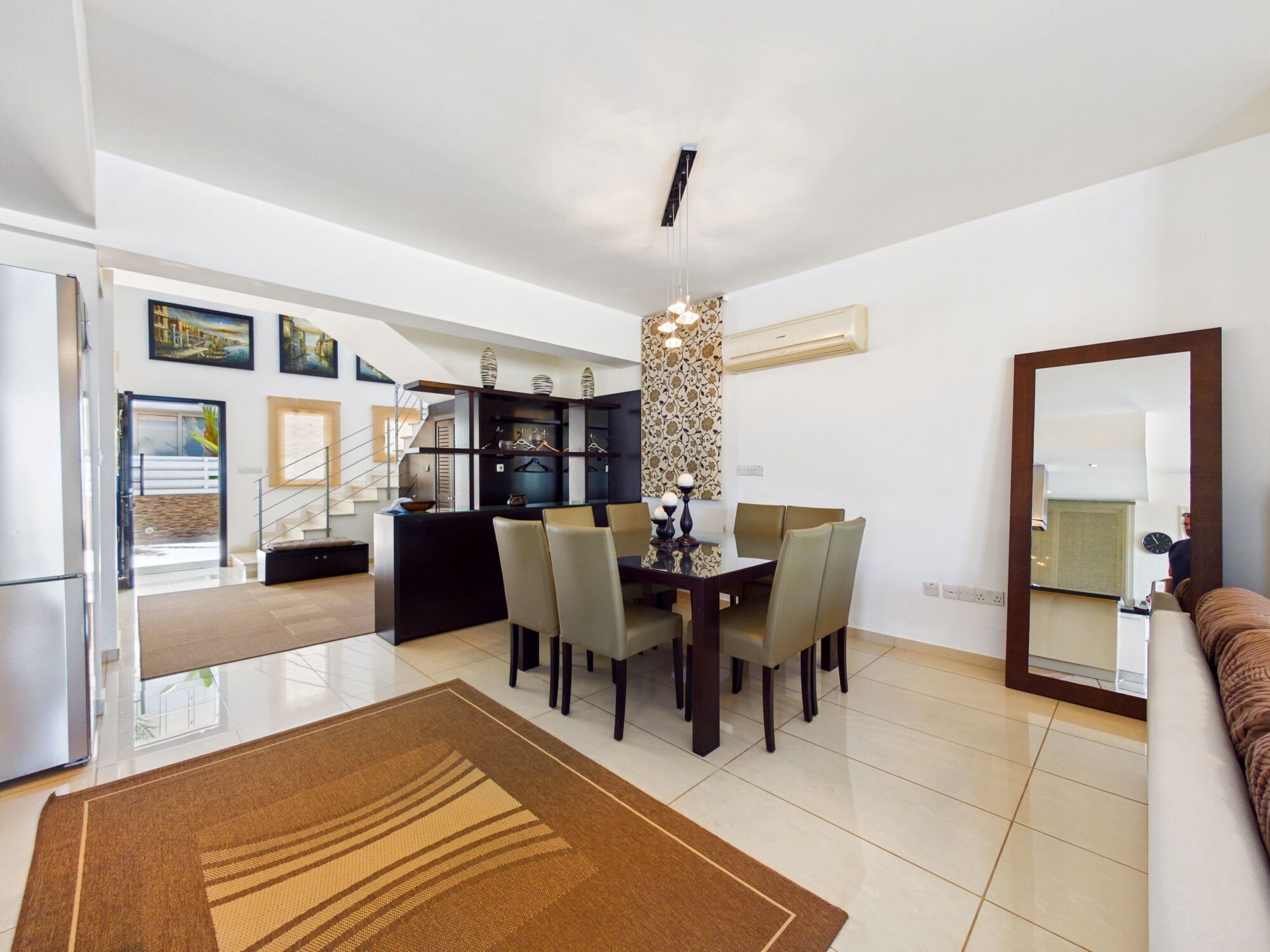 A modern living room with a dining area, kitchen, and a large mirror.