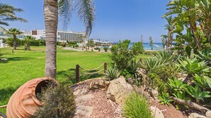 Ein angelegter Garten mit Palmen, einem Weg und Blick auf das Meer und Hotelgebäude.