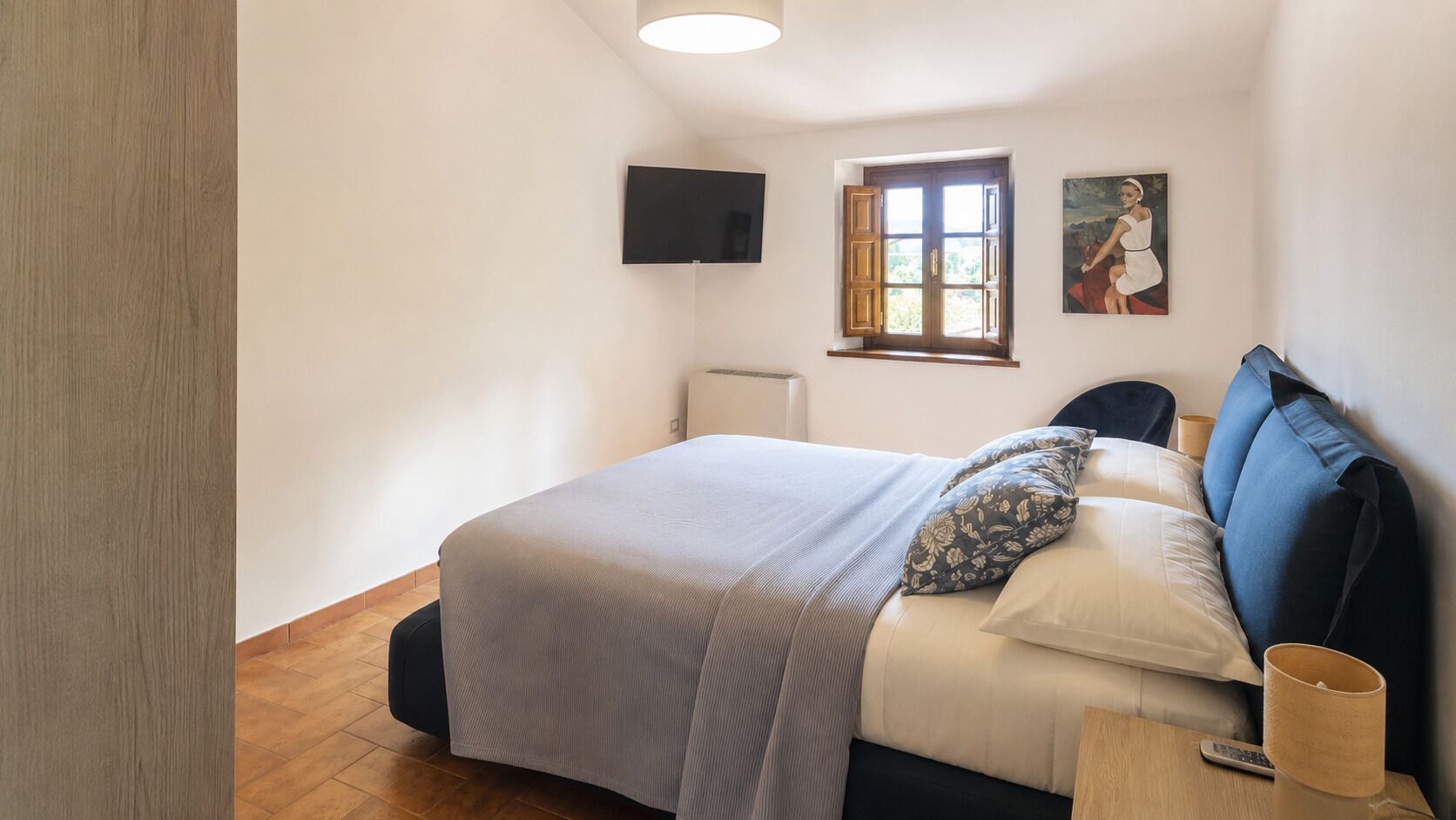 Un dormitorio con cama, ventana, un cuadro y un altavoz en la pared.