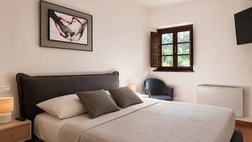 Ein Schlafzimmer mit einem Bett, einem Sessel, einem Fenster, einer Heizung und einem an der Wand hängenden Kunstwerk.