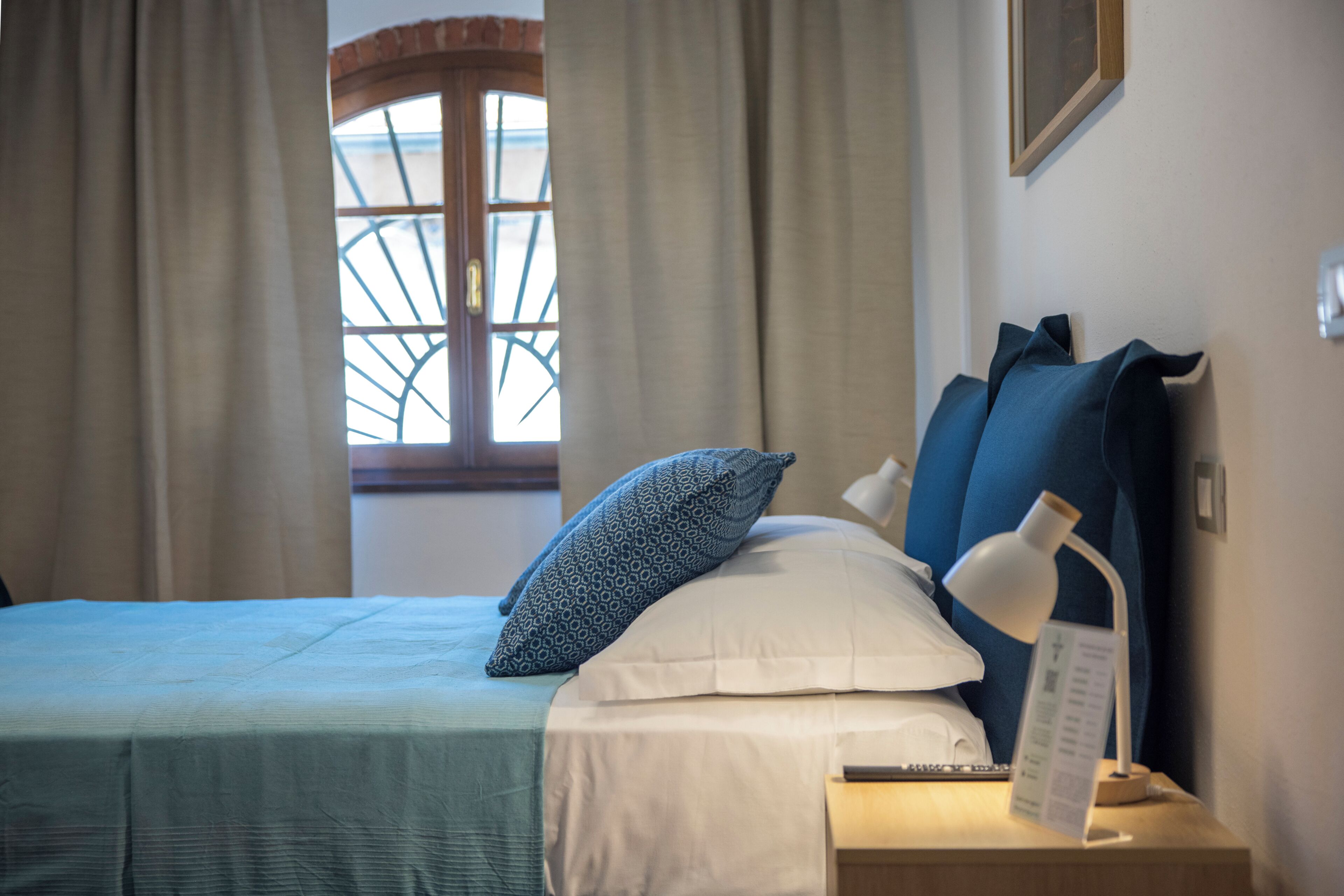 A bedroom with a bed, a nightstand, a lamp, and a window with curtains.