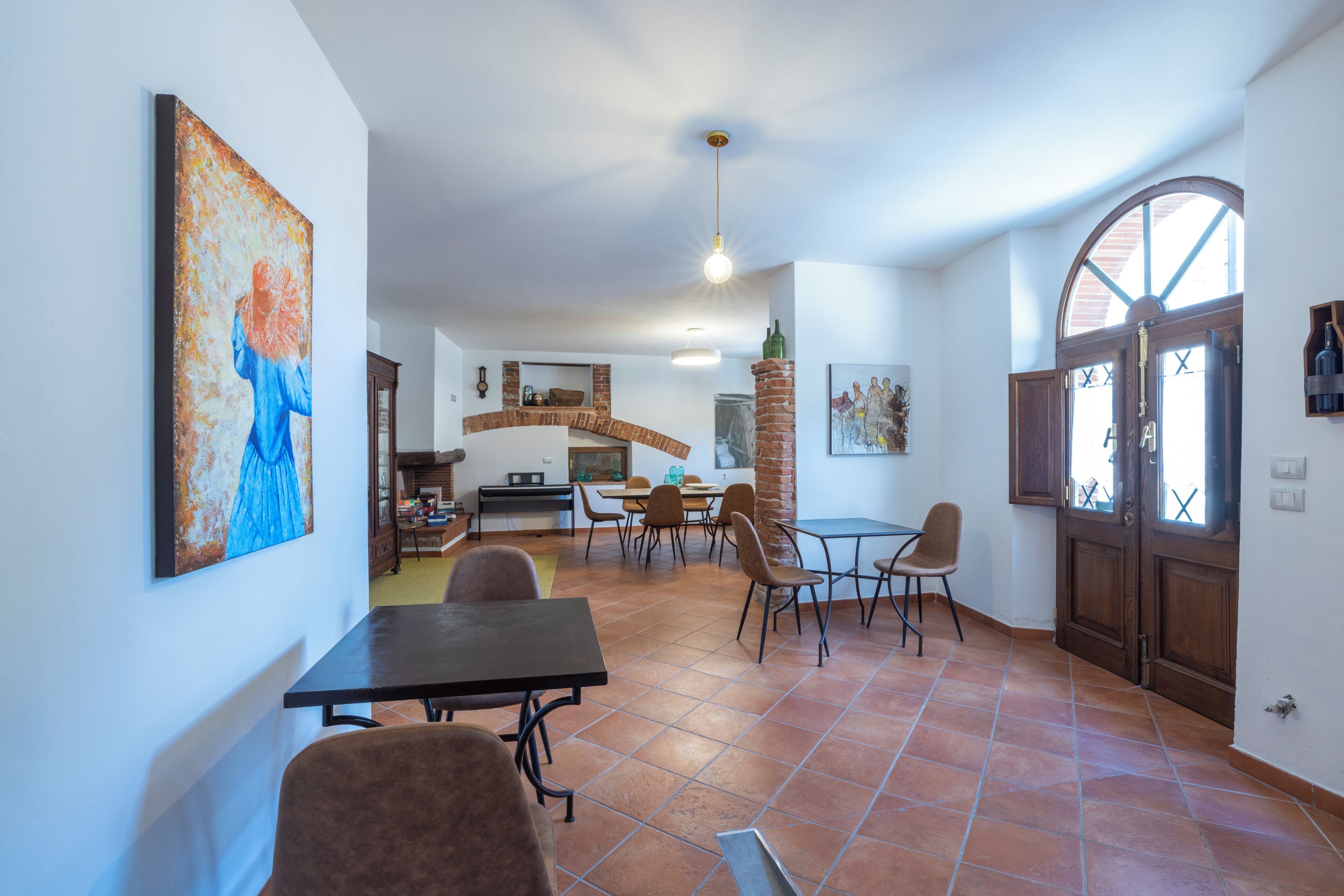 Un'ampia sala da pranzo con camino in mattoni, un grande quadro appeso e vista sulla cucina sullo sfondo.