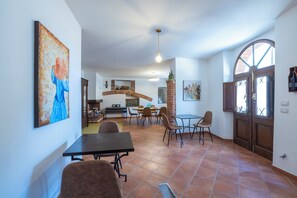 A spacious dining area with a brick fireplace, a large painting on the wall, and a view of the kitchen in the background.