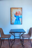 Una habitación con una mesa, dos sillas, un cuadro en la pared y piso de baldosas.