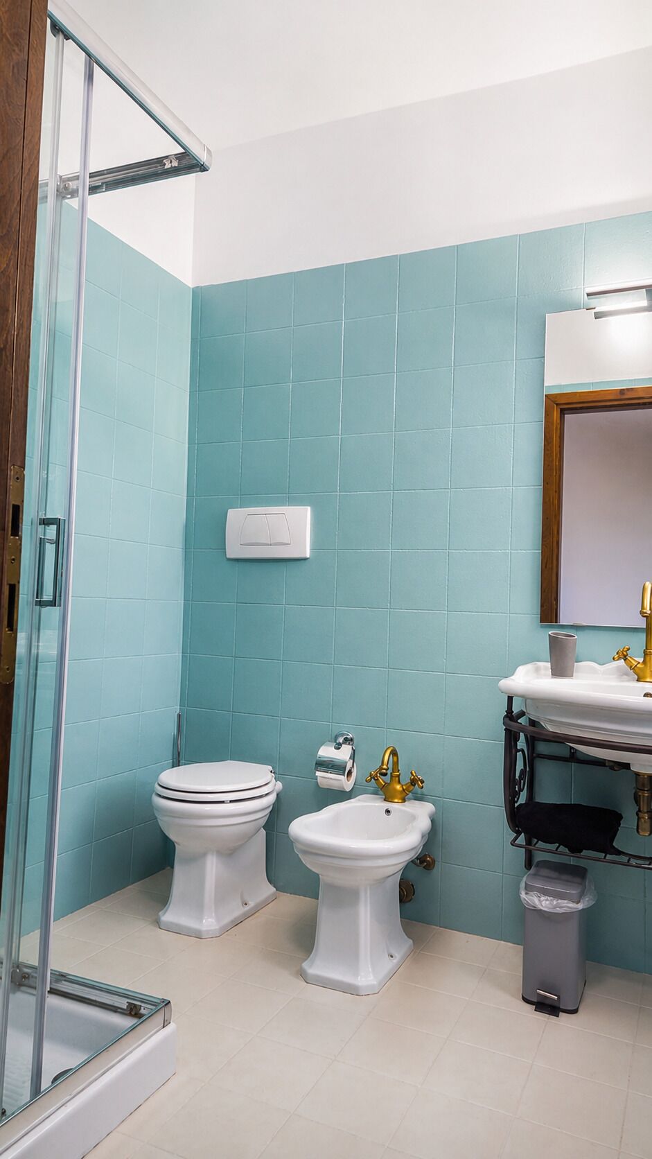 A bathroom with two toilets, a sink, a mirror, and a trash bin.