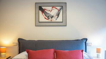 Un dormitorio con una cama, dos almohadas rojas, una obra de arte enmarcada sobre la cama y lámparas de noche.
