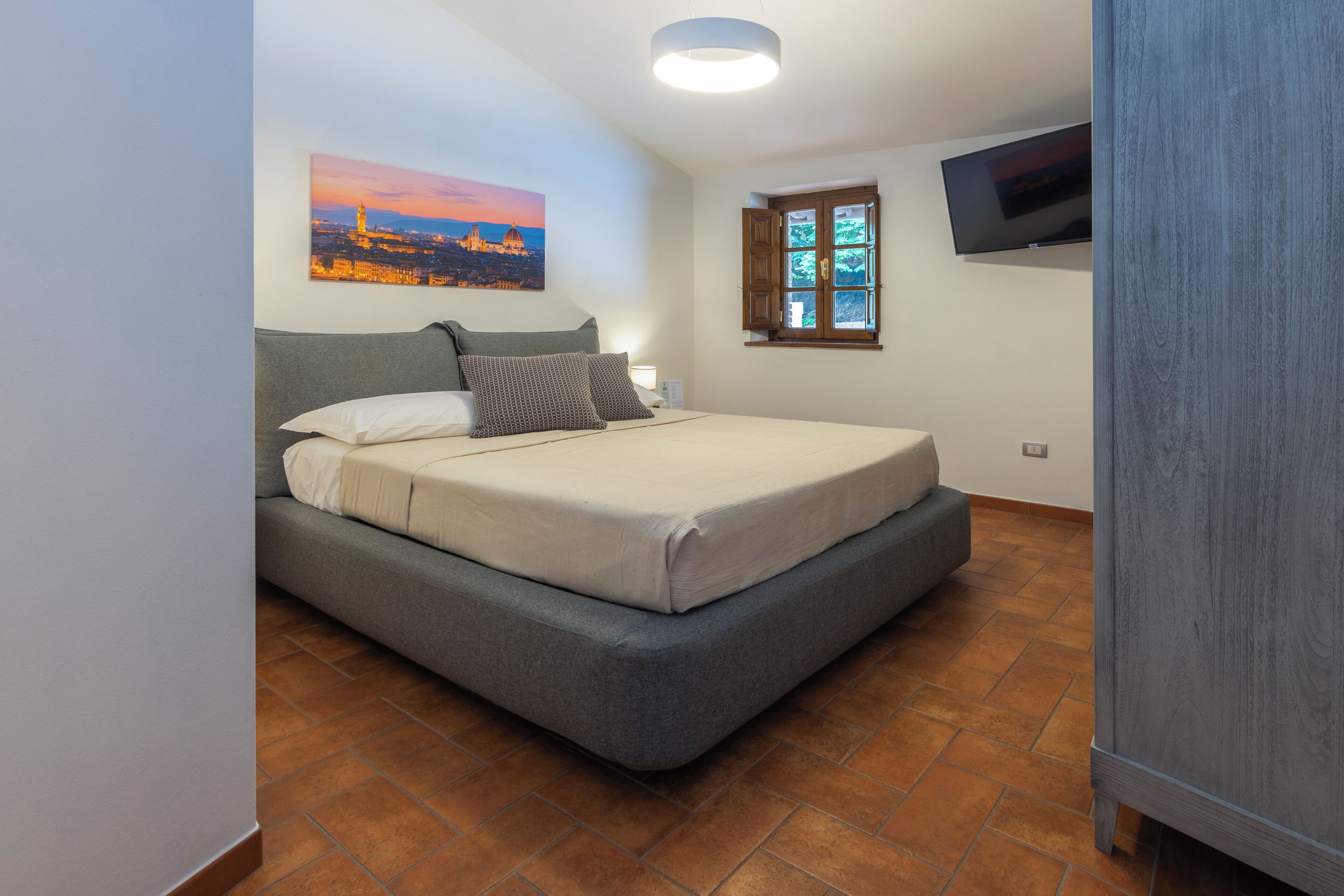 Una camera da letto con un letto, una finestra vista, un quadro appeso al muro e una televisione a parete.