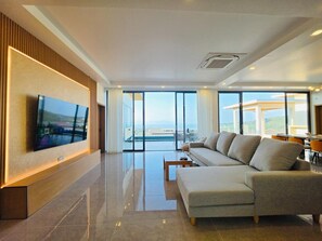 Ein modernes Wohnzimmer mit großem Flachbildfernseher, einer Couch, einem Couchtisch und Meerblick durch große Fenster.