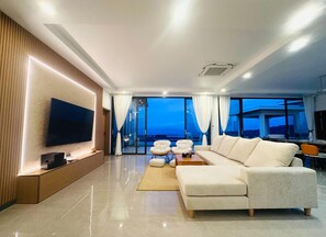Ein modernes Wohnzimmer mit großem Flachbildfernseher, einem Ecksofa und einem Essbereich mit Tisch und Stühlen.