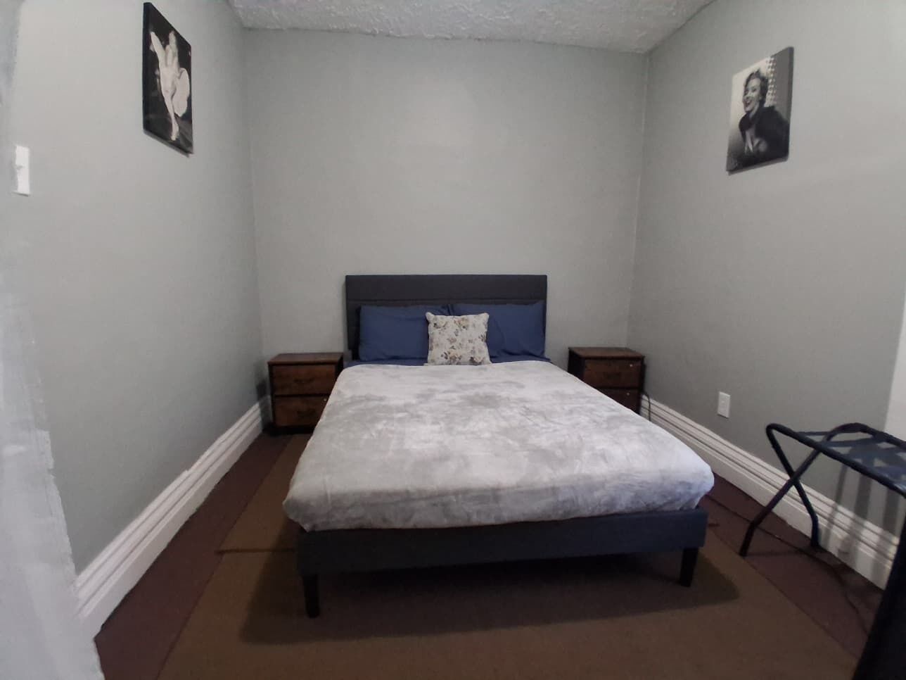 Een slaapkamer met een bed, nachtkastjes, een stoel en twee ingelijste foto’s aan de muur.