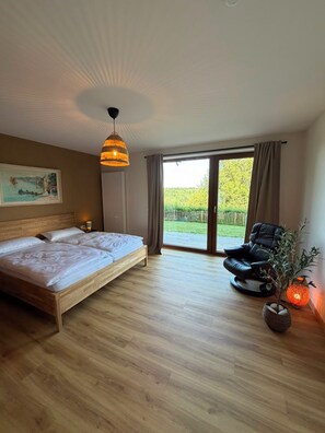 Een slaapkamer met een groot bed, een massagestoel, een kamerplant en uitzicht op de omgeving.