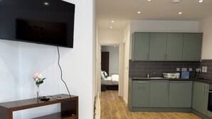 Una cocina moderna con gabinetes verdes, piso de madera y televisor de pantalla plana montado en la pared.