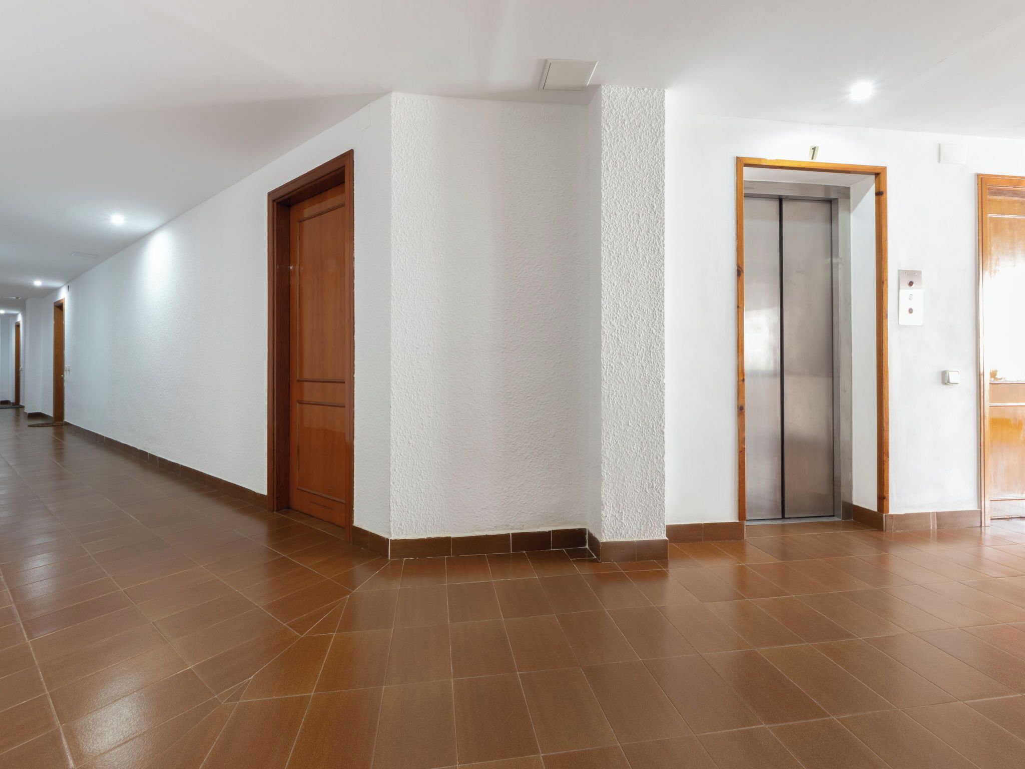 A corridor with a wooden door, a textured wall, and an elevator.